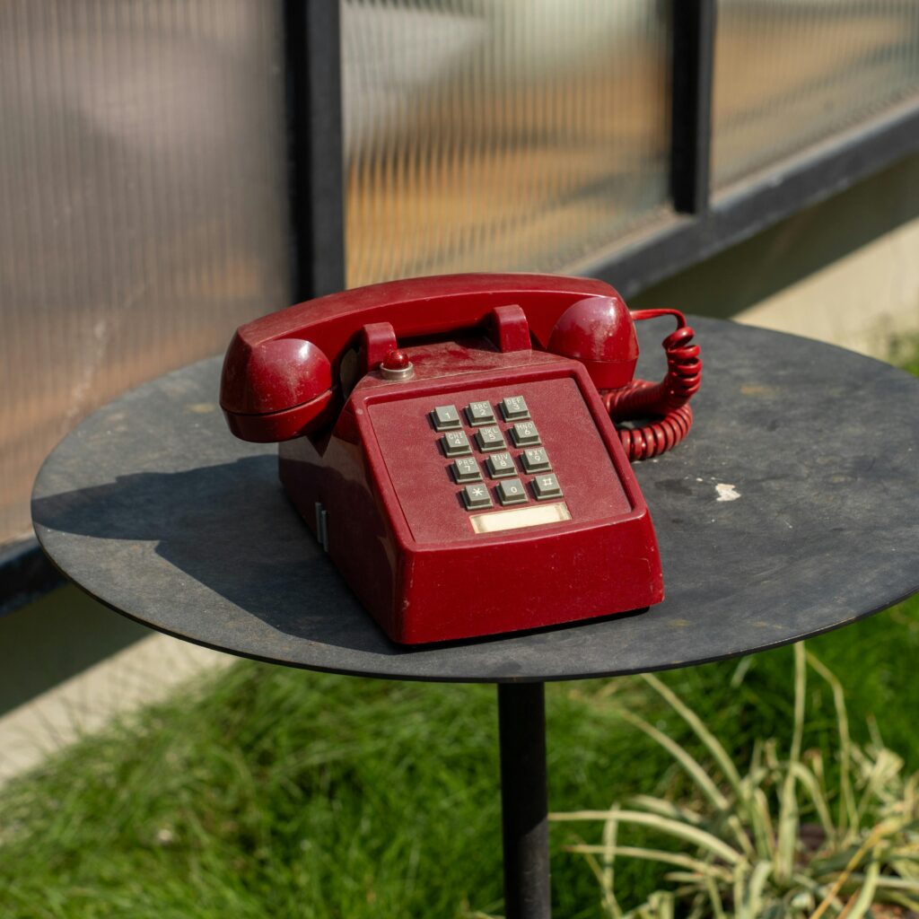 A red telephone on a table next to a window